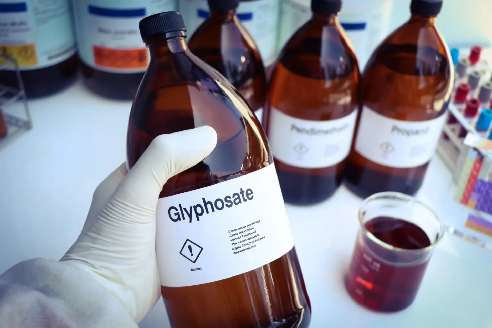 Gloved hand holding a bottle labeled Glyphosate in a lab.