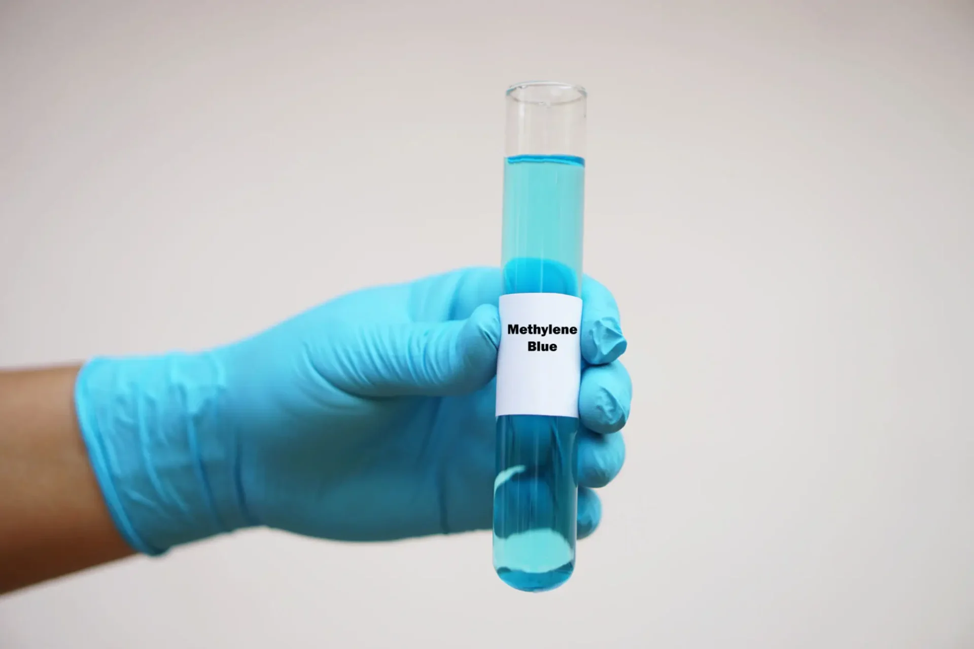 Gloved hand holding a test tube with blue liquid labeled 'methanol'.