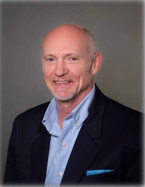 Professional headshot of a smiling bald man in a suit jacket and light blue shirt.