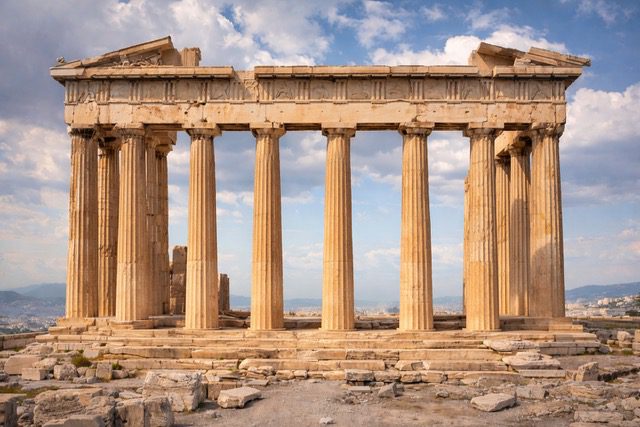 Ancient Greek temple ruins with tall stone columns under a blue sky.