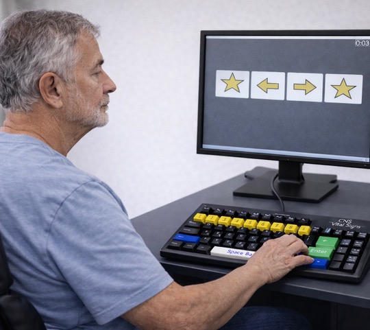 An elderly man uses a specialized computer with large buttons and a screen showing star images.